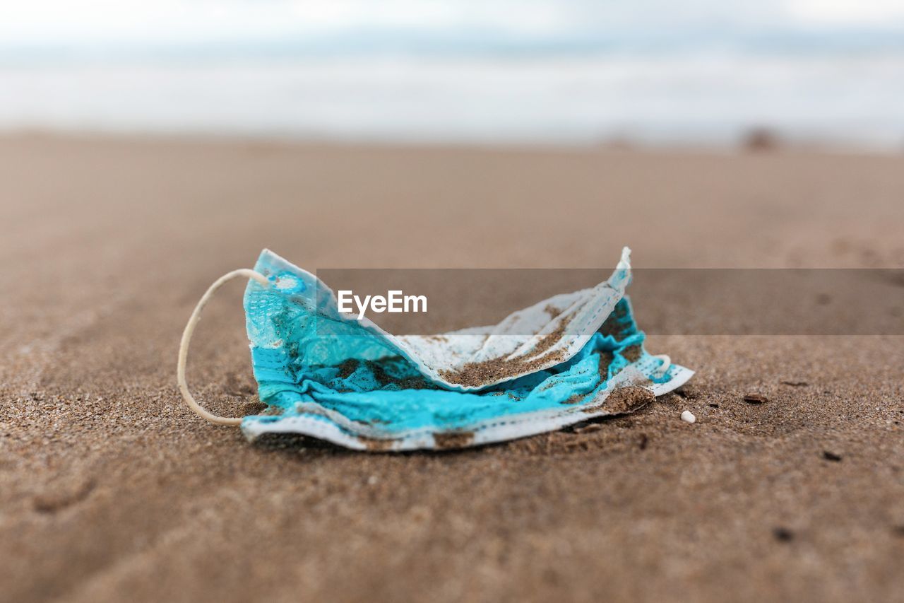 Used protective mask on beach washed by sea wave showing concept of environmental pollution with medical waste