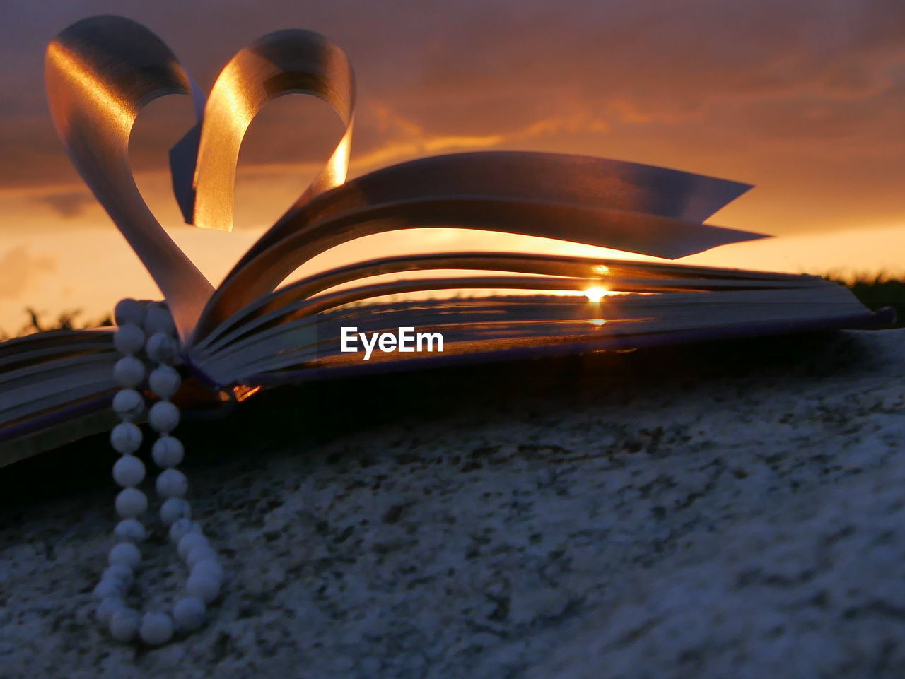 Bead necklace with heart shape folded pages of book during sunset