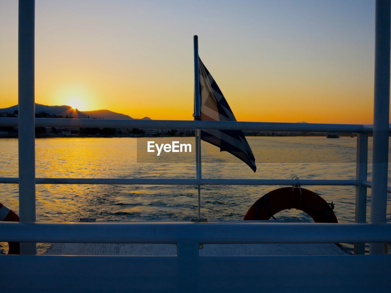 Flag on boat sailing in sea against clear sky during sunset