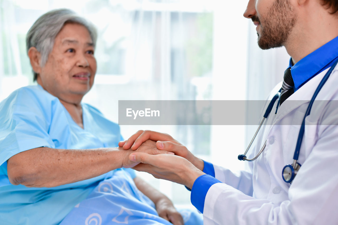 Midsection of doctor holding patient hand in hospital