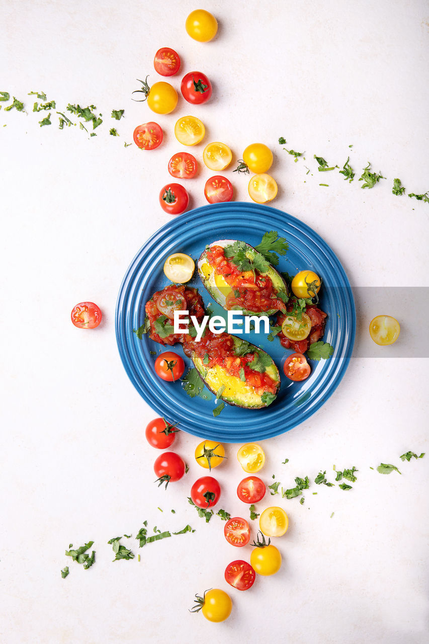 High angle view of egg in avocado with cherry tomatoes served in plate on table