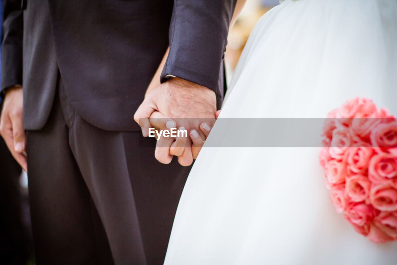 MIDSECTION OF COUPLE HOLDING HANDS IN DRESS