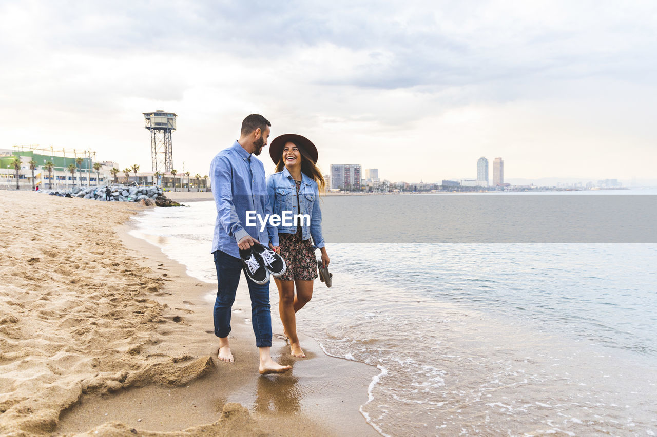 Spain, barcelona, couple walking barefoot on the beach