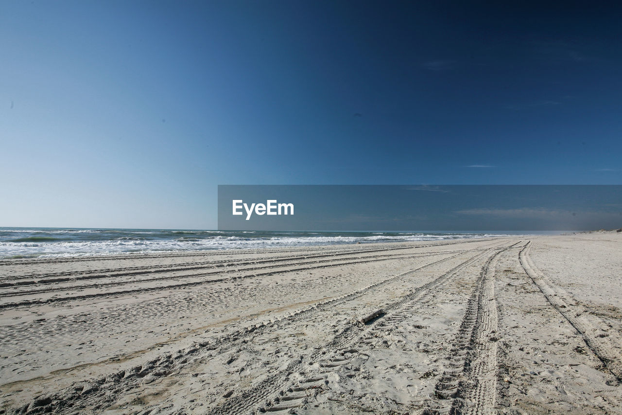 TIRE TRACKS ON BEACH AGAINST BLUE SKY