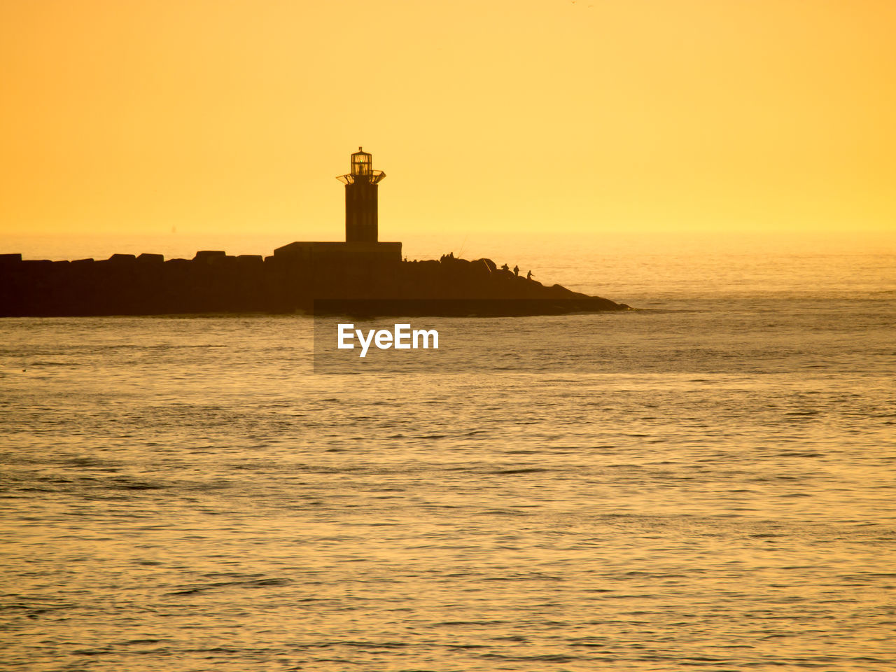 LIGHTHOUSE BY SEA AGAINST ORANGE SKY