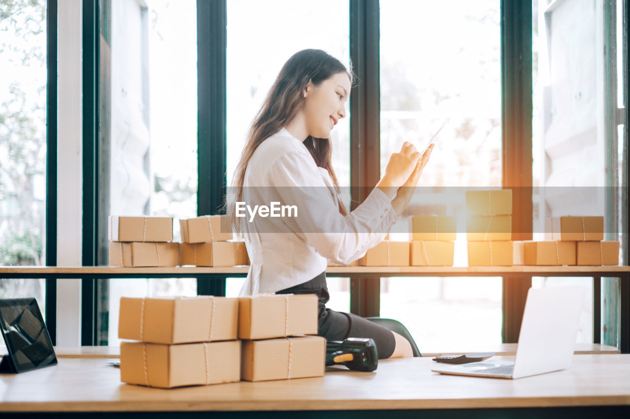 Young businesswoman working while sitting by packages at office