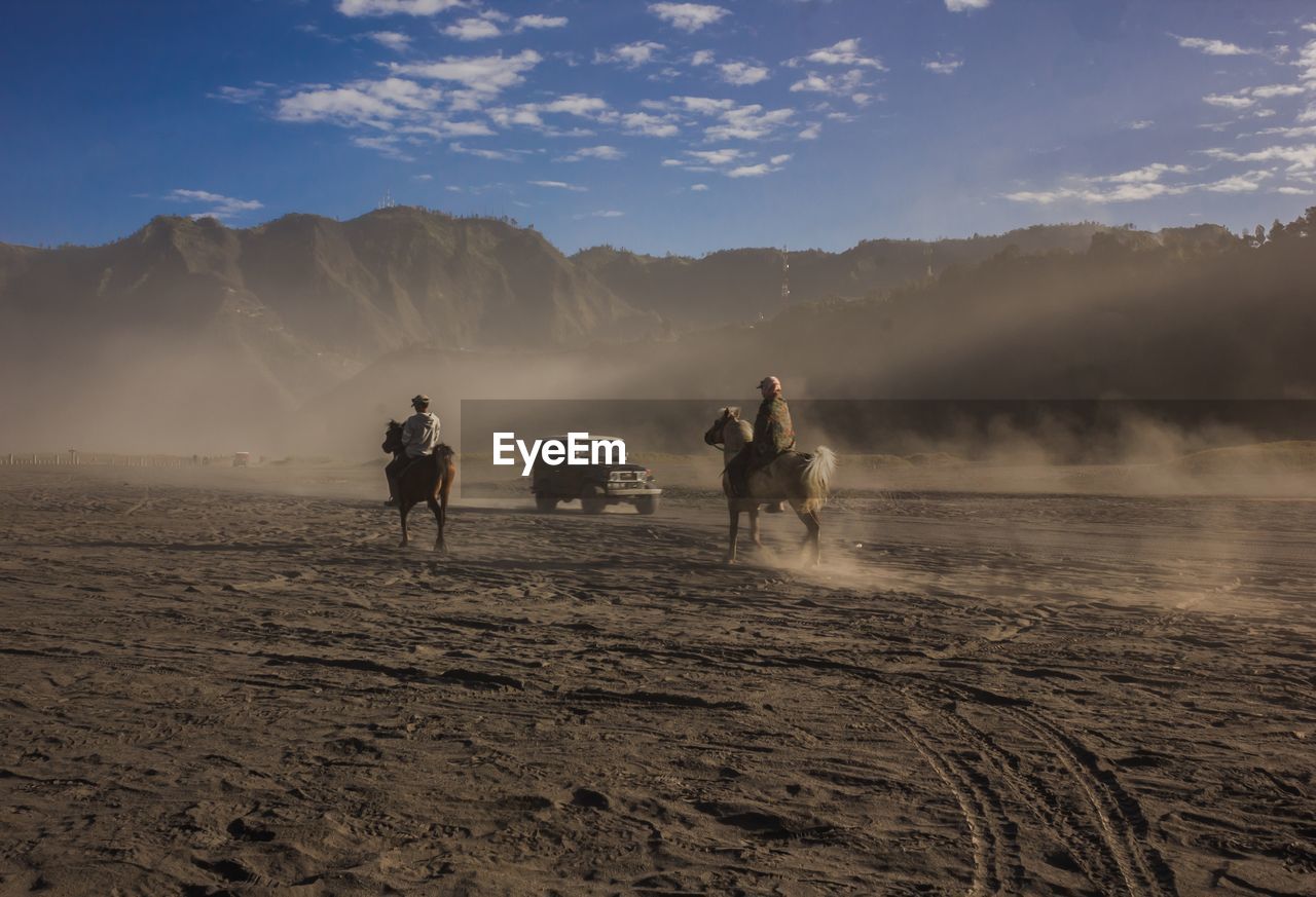 People riding horses on land against sky