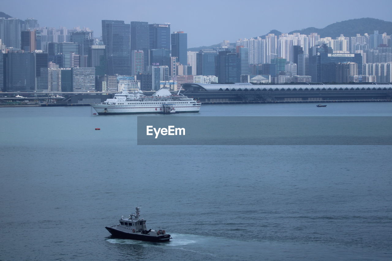 Boats in sea by buildings at city against sky