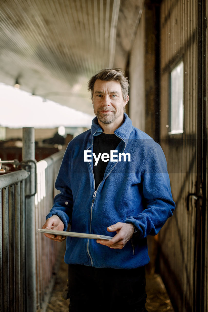 Smiling farmer with digital tablet standing at cattle farm