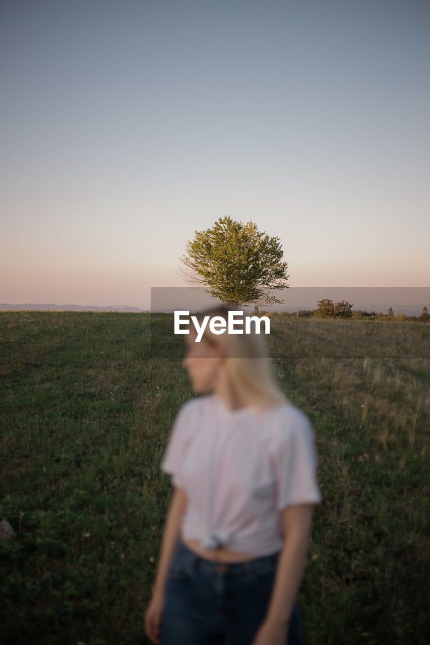 A young woman standing in a field during sunset