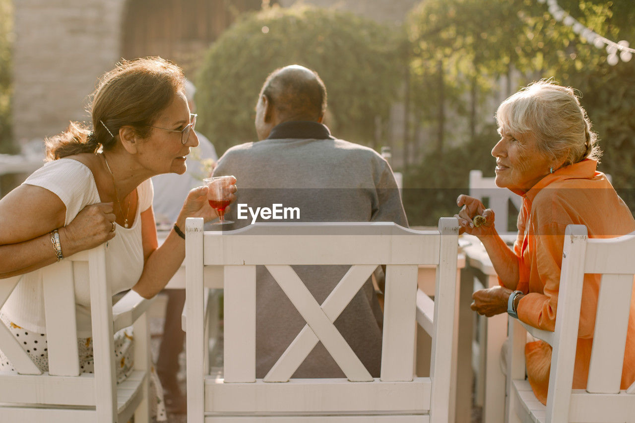 Retired senior women talking behind man while sitting at back yard