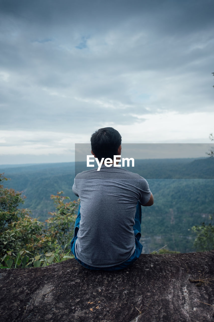 REAR VIEW OF MAN SITTING ON MOUNTAIN