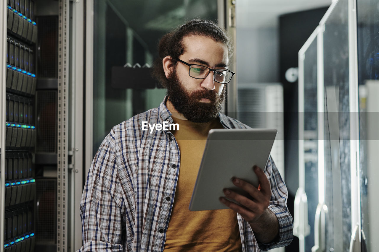 Technician wearing eyeglasses looking at tablet pc in server room