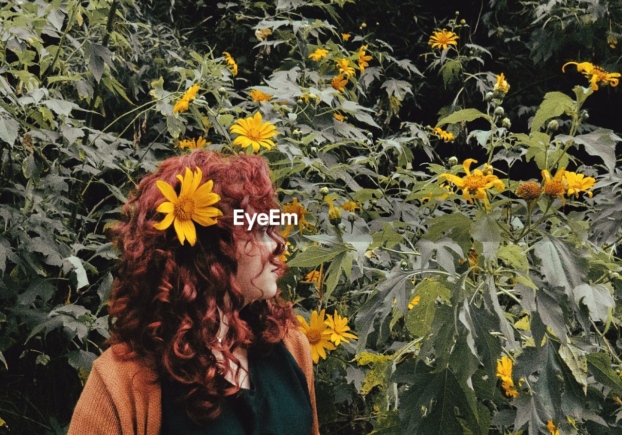 Redhead woman standing by yellow flowers blooming outdoors