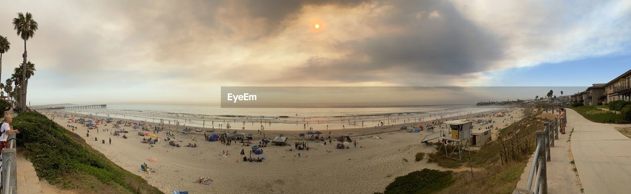 HIGH ANGLE VIEW OF CROWD ON BEACH AGAINST SKY