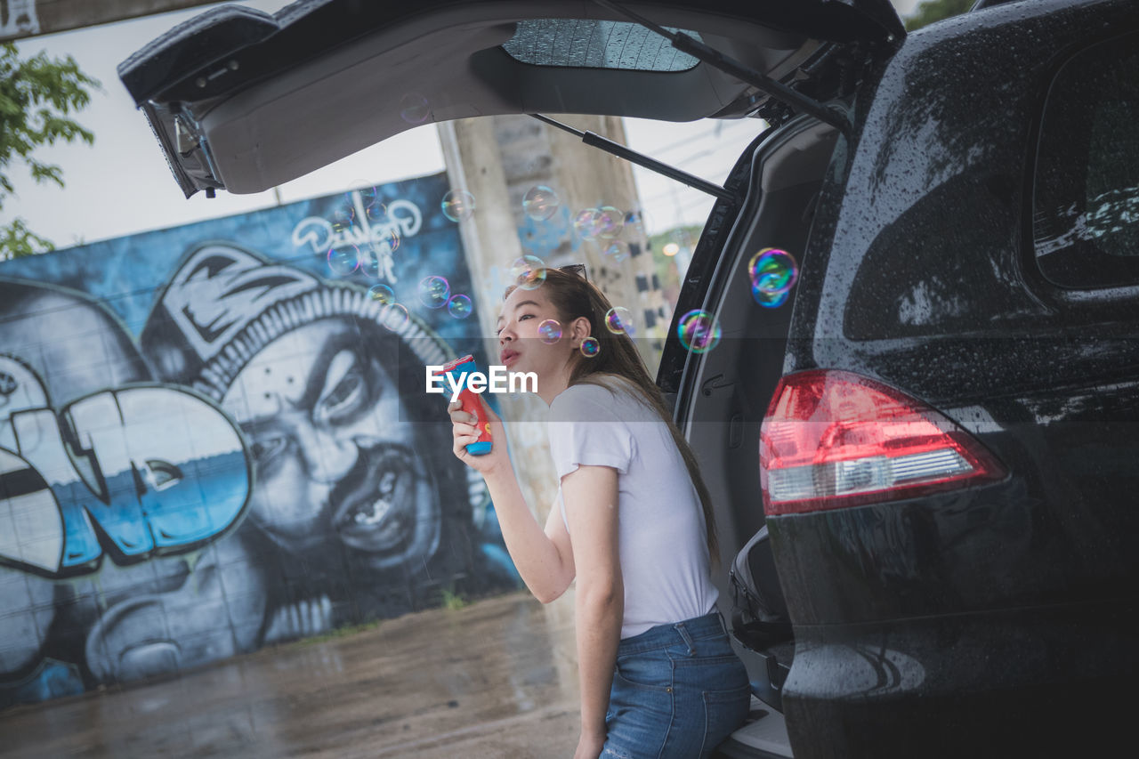 FULL LENGTH OF WOMAN WITH GRAFFITI ON CAR