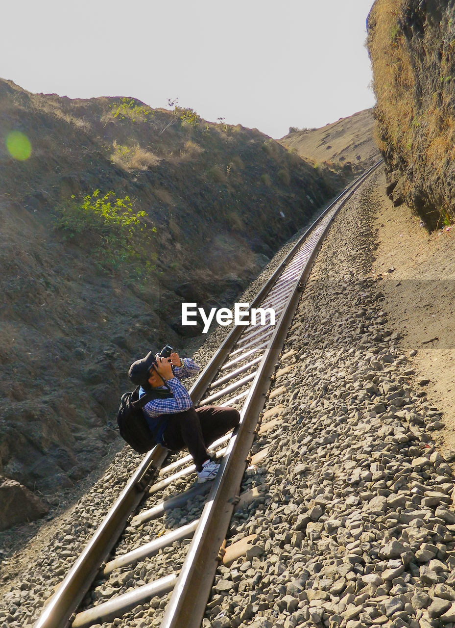 Full length of man photographing through camera while crouching on railroad track