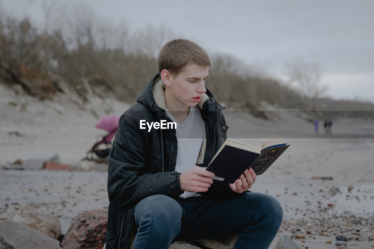 Teenager sits on the beach reads a book, looks into a textbook. immersed in the study of the materia