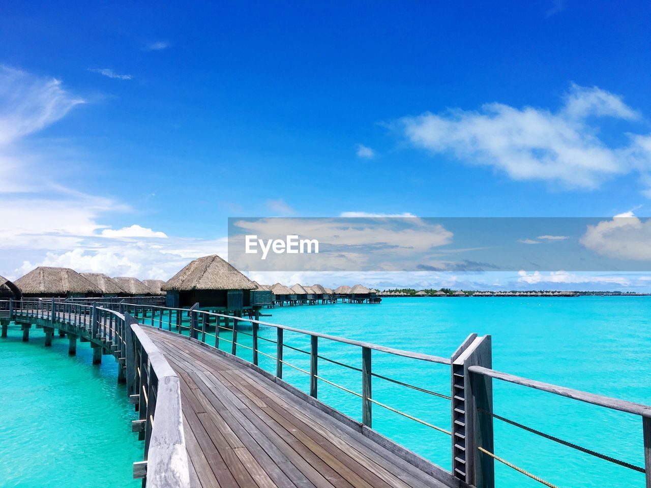 Pier by bungalows on lagoon against sky at bora bora island