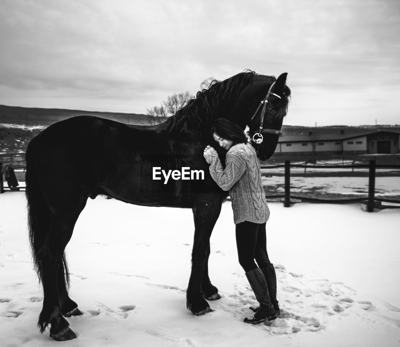 Full length of woman embracing horse on snow covered land