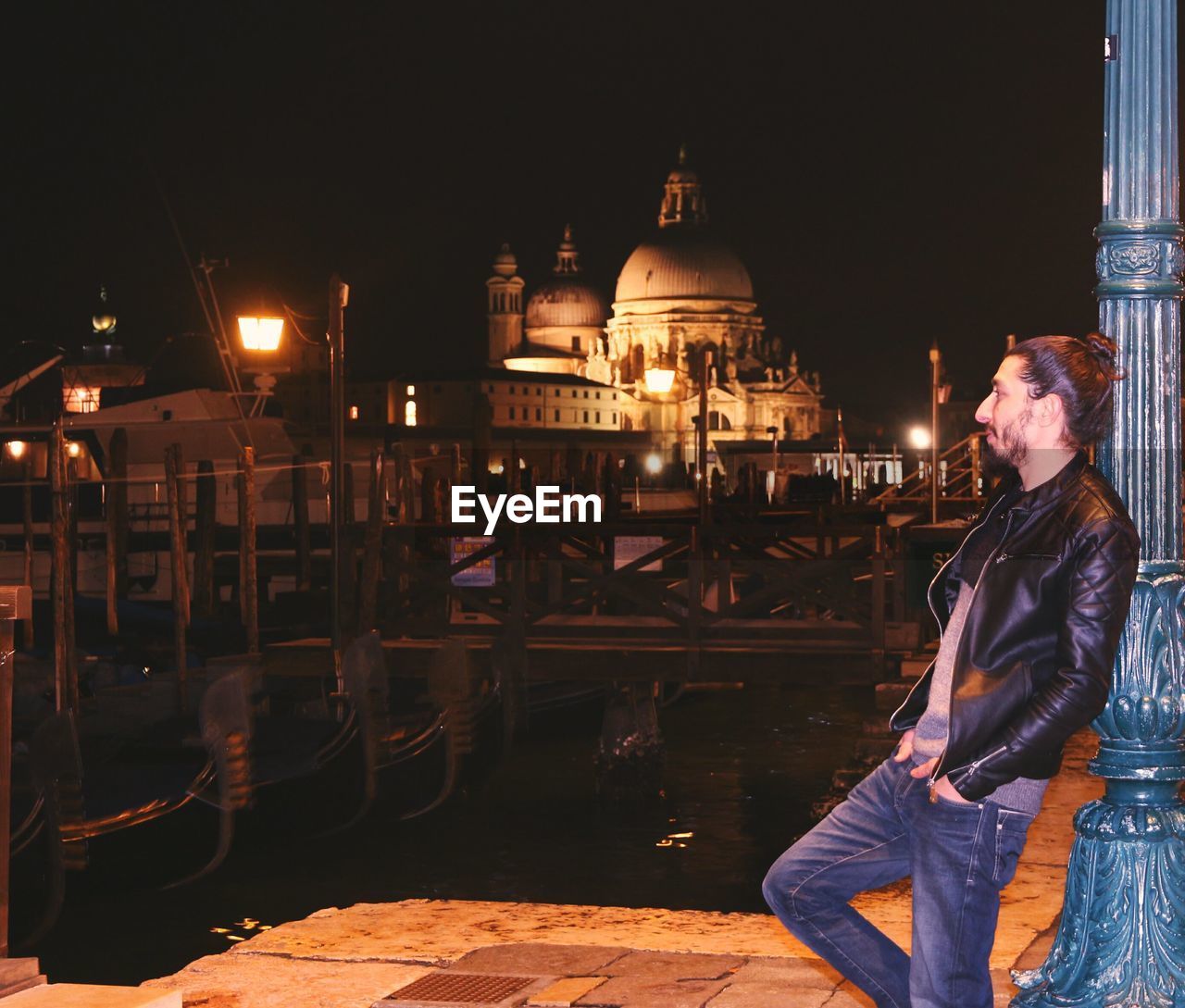 Young man standing on footpath by grand canal against santa maria della salute at night