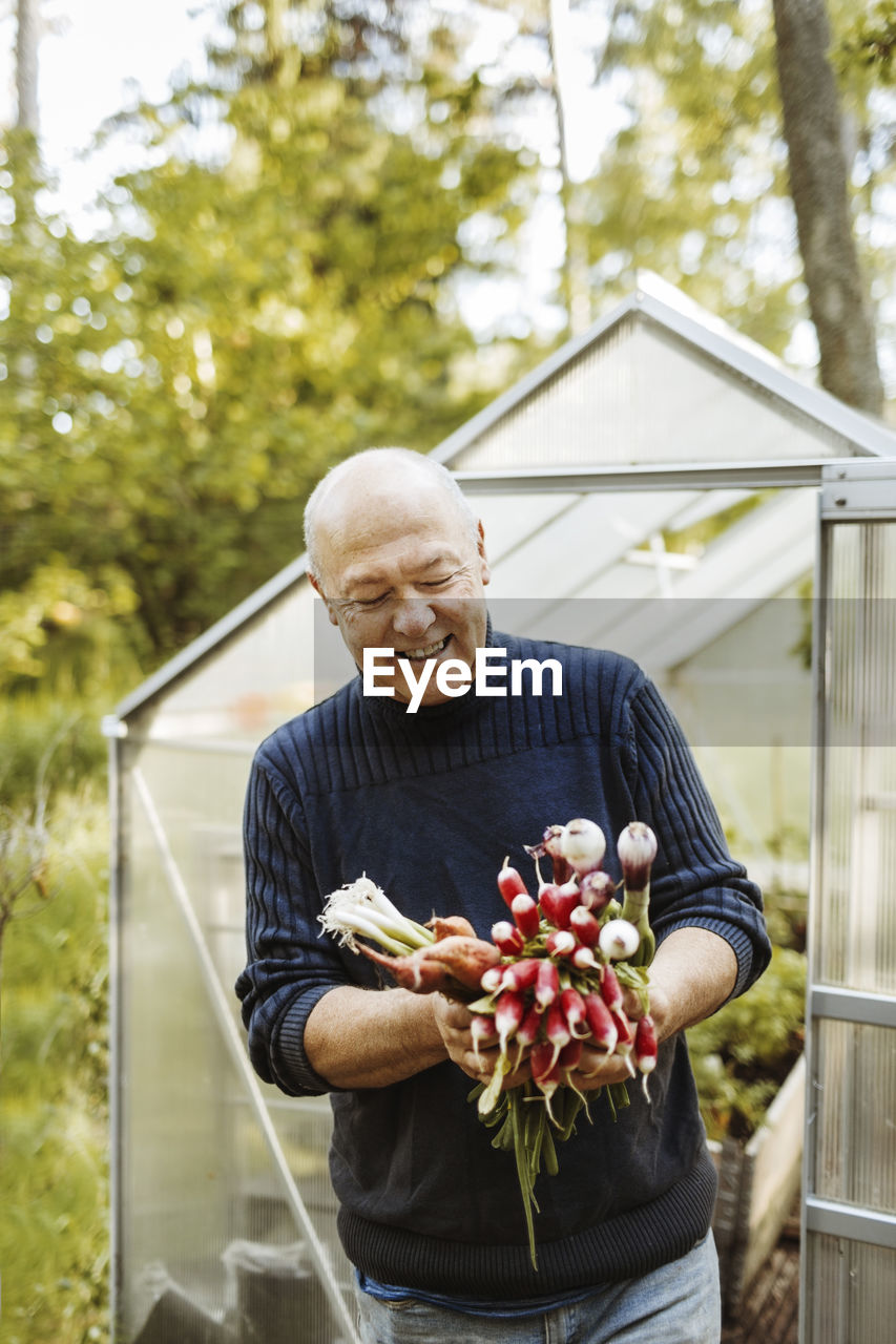 Happy gay man holding fresh root vegetables at garden