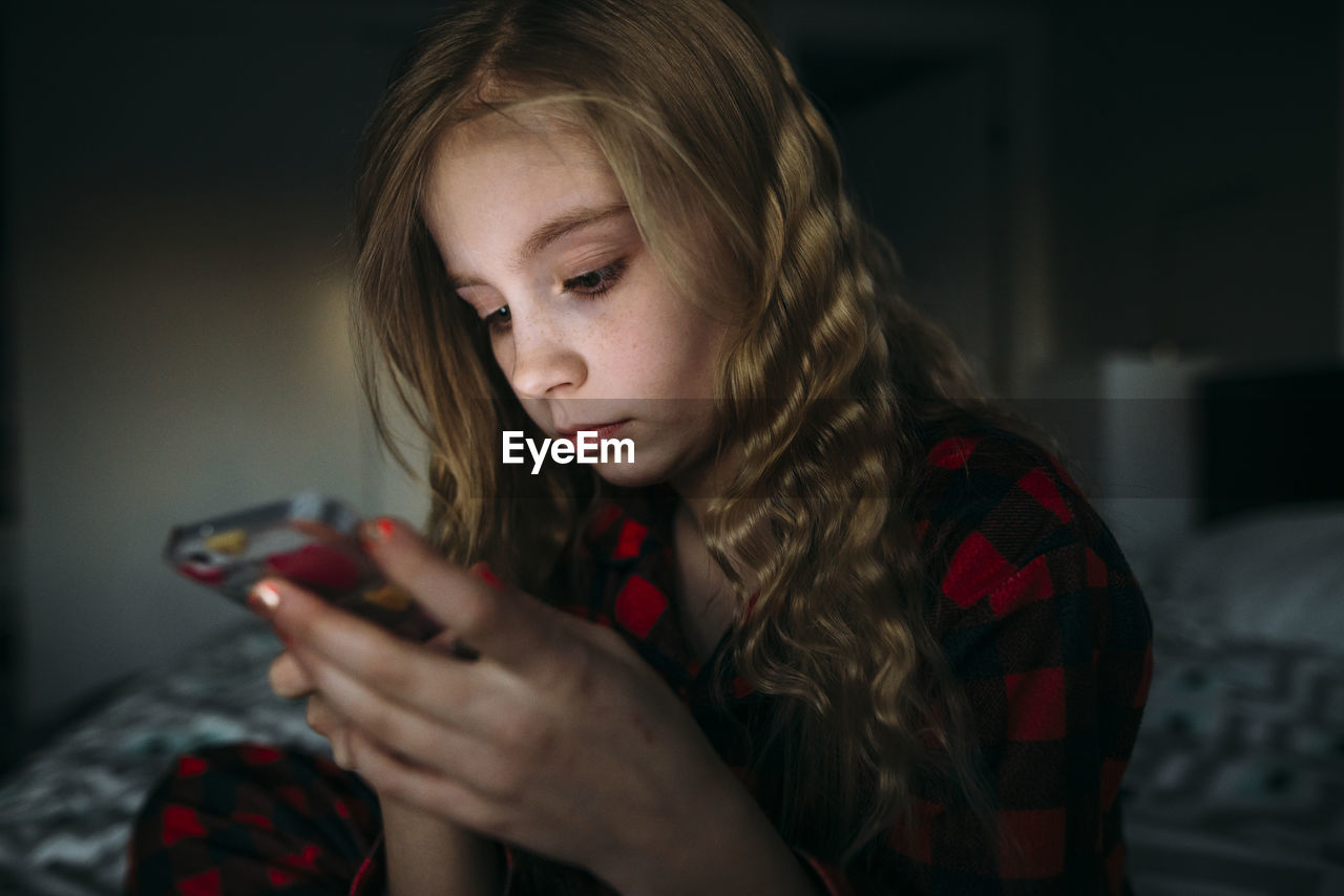 Close-up of girl using mobile phone while sitting on bed at home