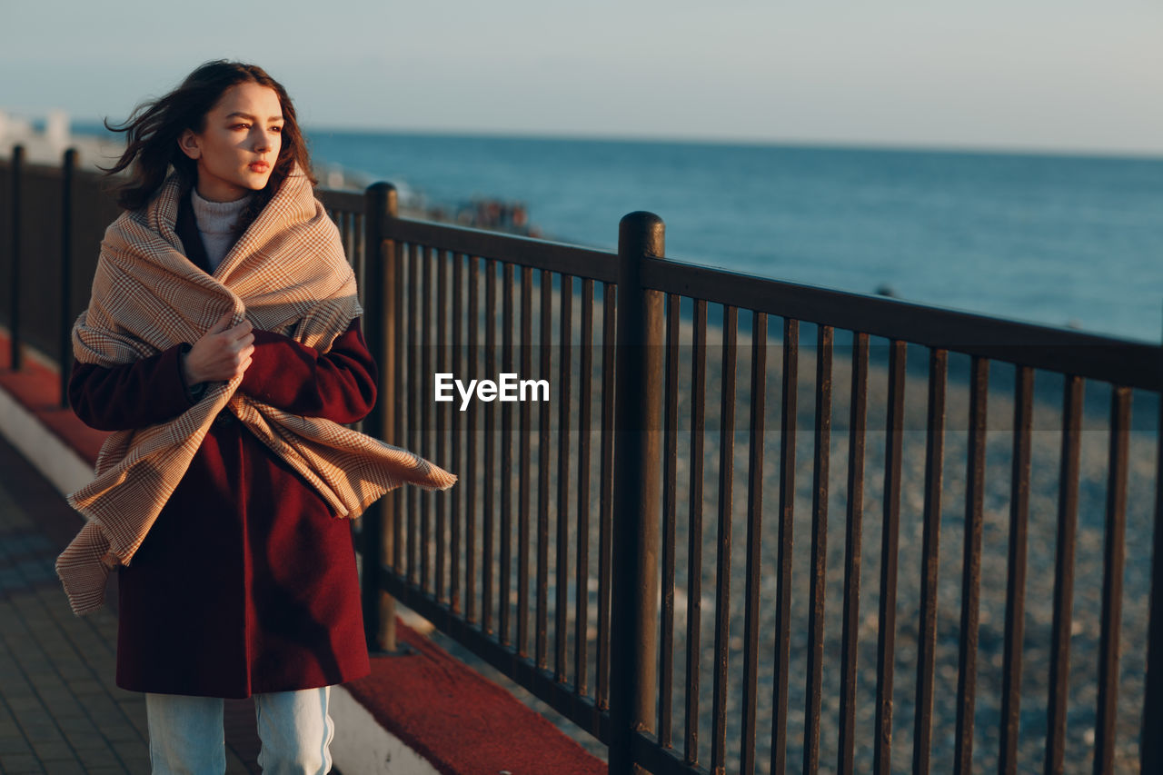 BEAUTIFUL WOMAN STANDING BY RAILING AGAINST SEA