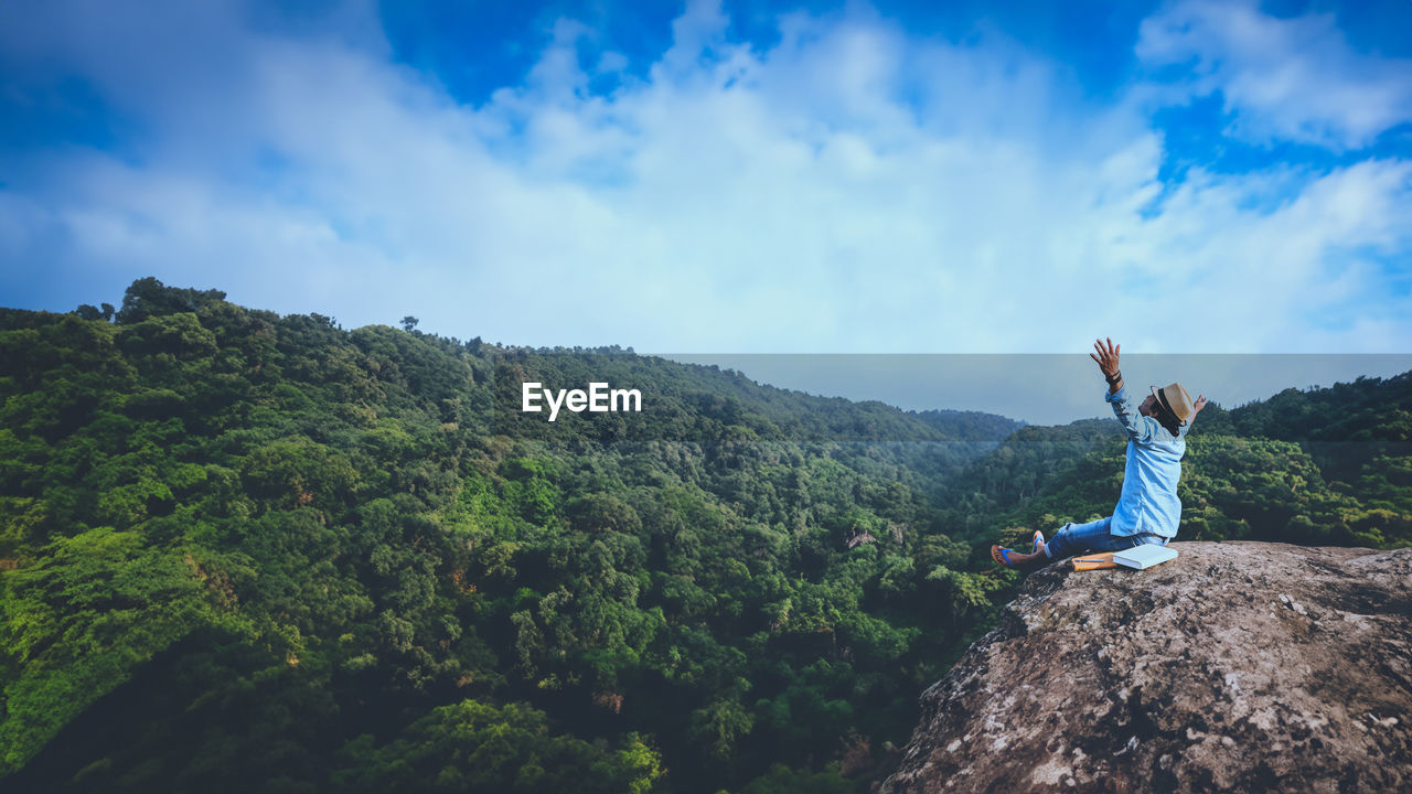 rear view of woman standing on rock against sky