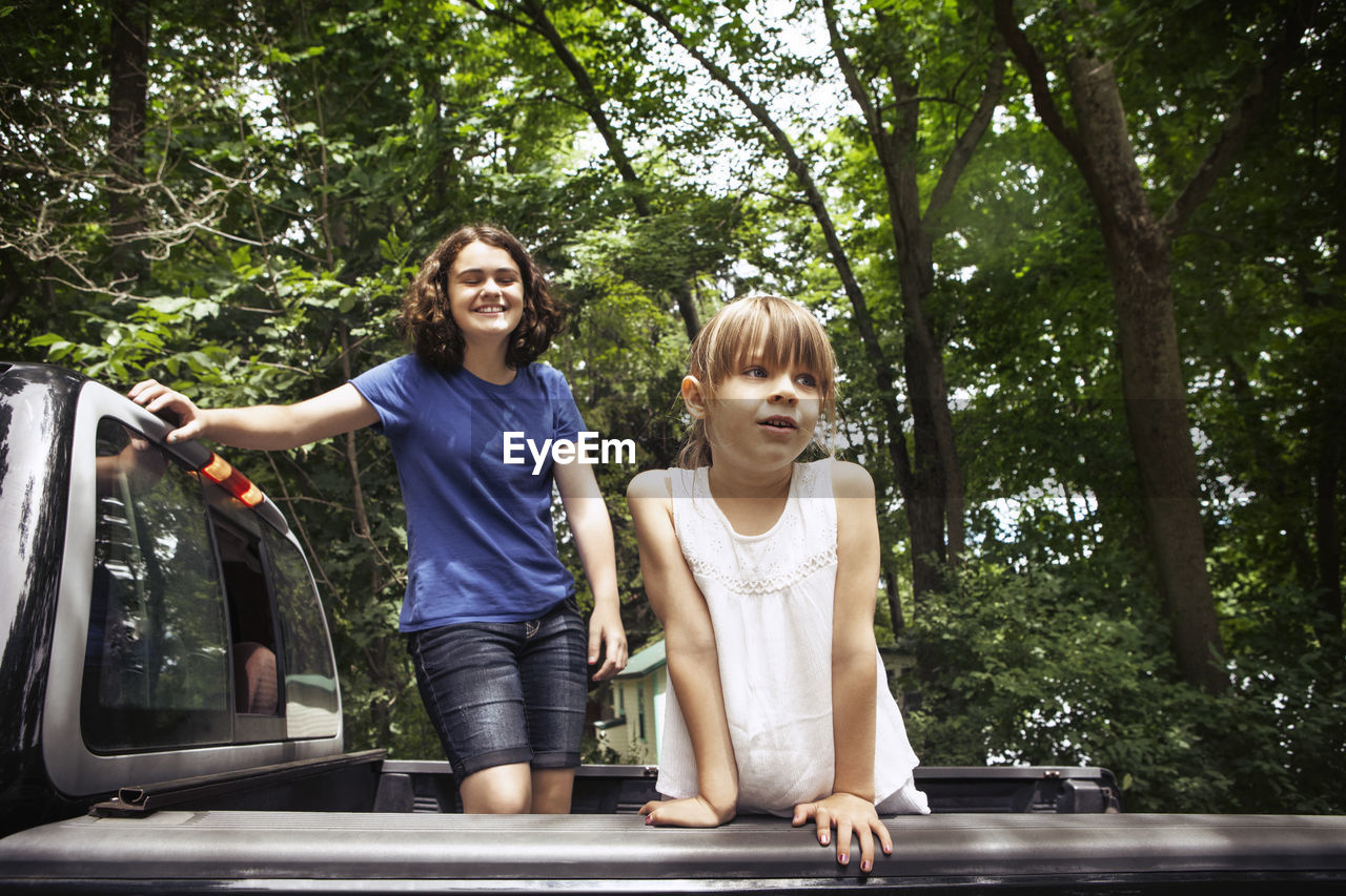 Sisters standing in pick-up truck against trees