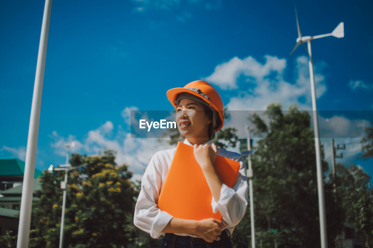 Low angle view of female engineer standing against windmill