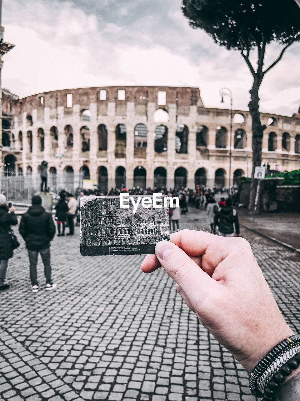 Cropped hand of man holding photograph against historical building