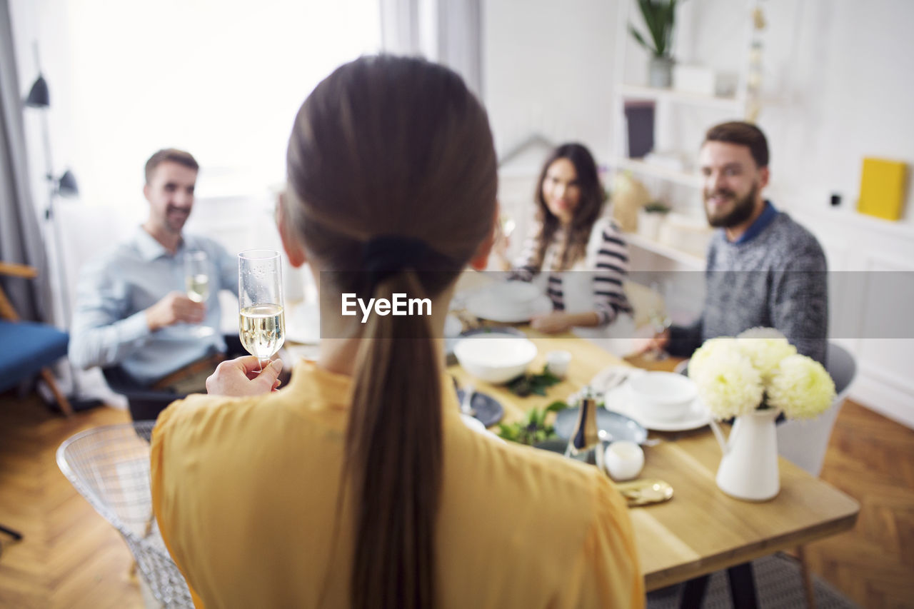 Rear view of woman holding champagne flute while friends sitting at table