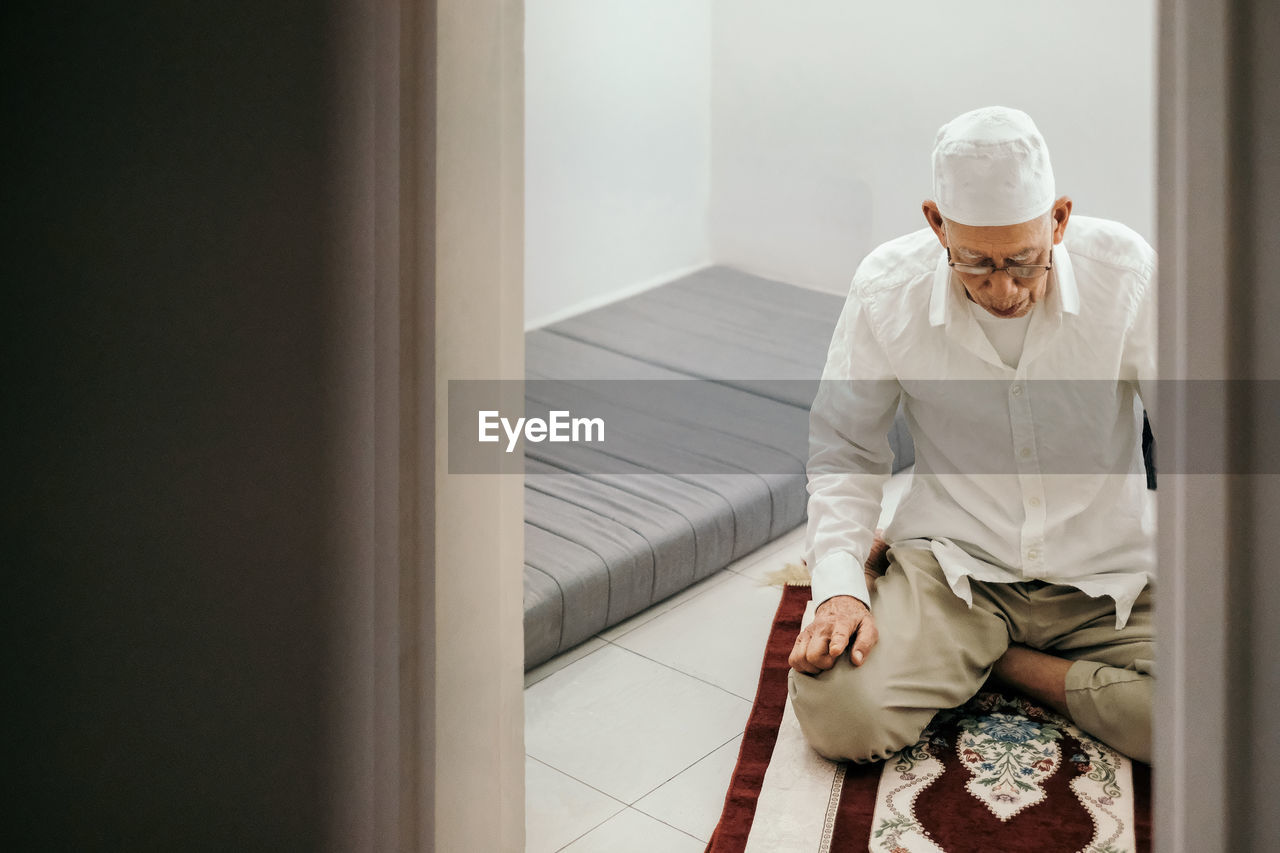 Senior man praying at home seen through doorway