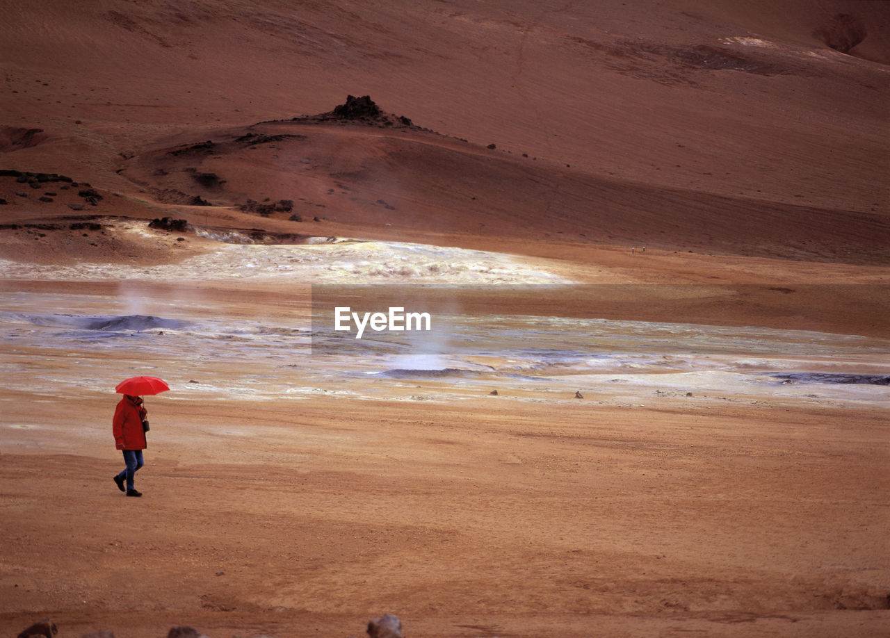 Woman walking with red umbrella at namskard geothermal hot spring area