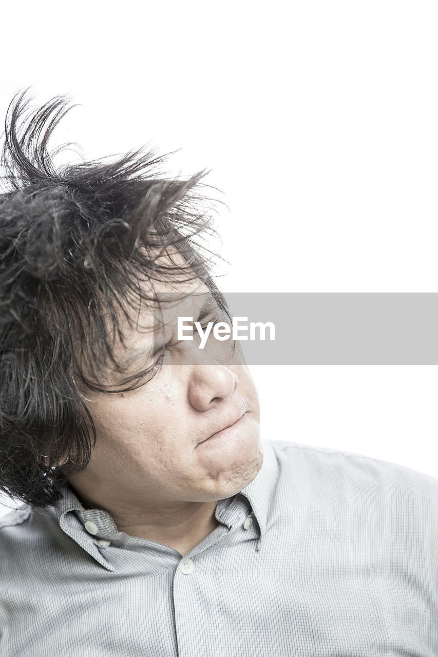 Close-up of frustrated man tossing hair against white background