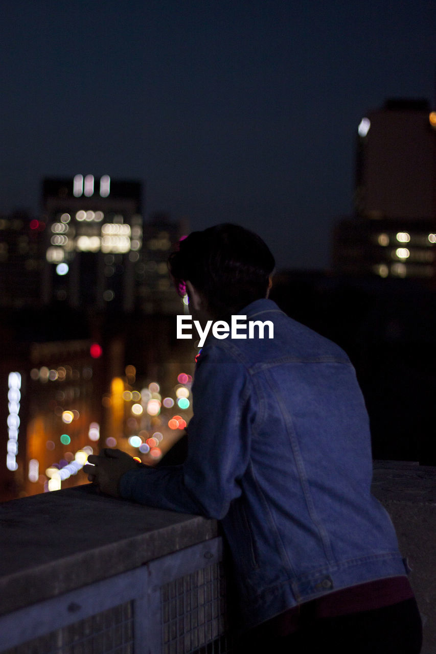 Rear view of man standing on terrace in city at night