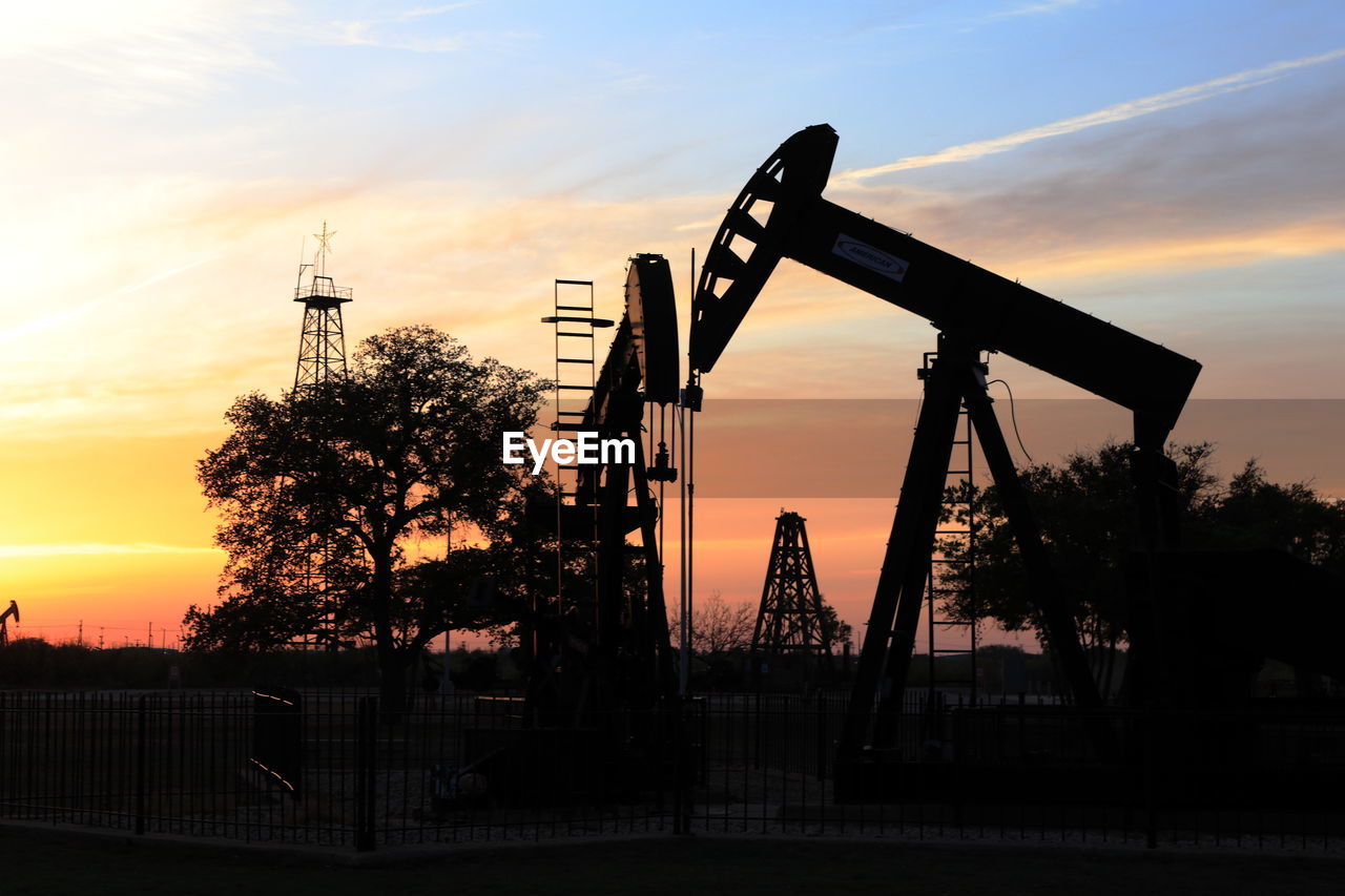 Pump jacks and drilling rig at sunset, oilfield silhouette