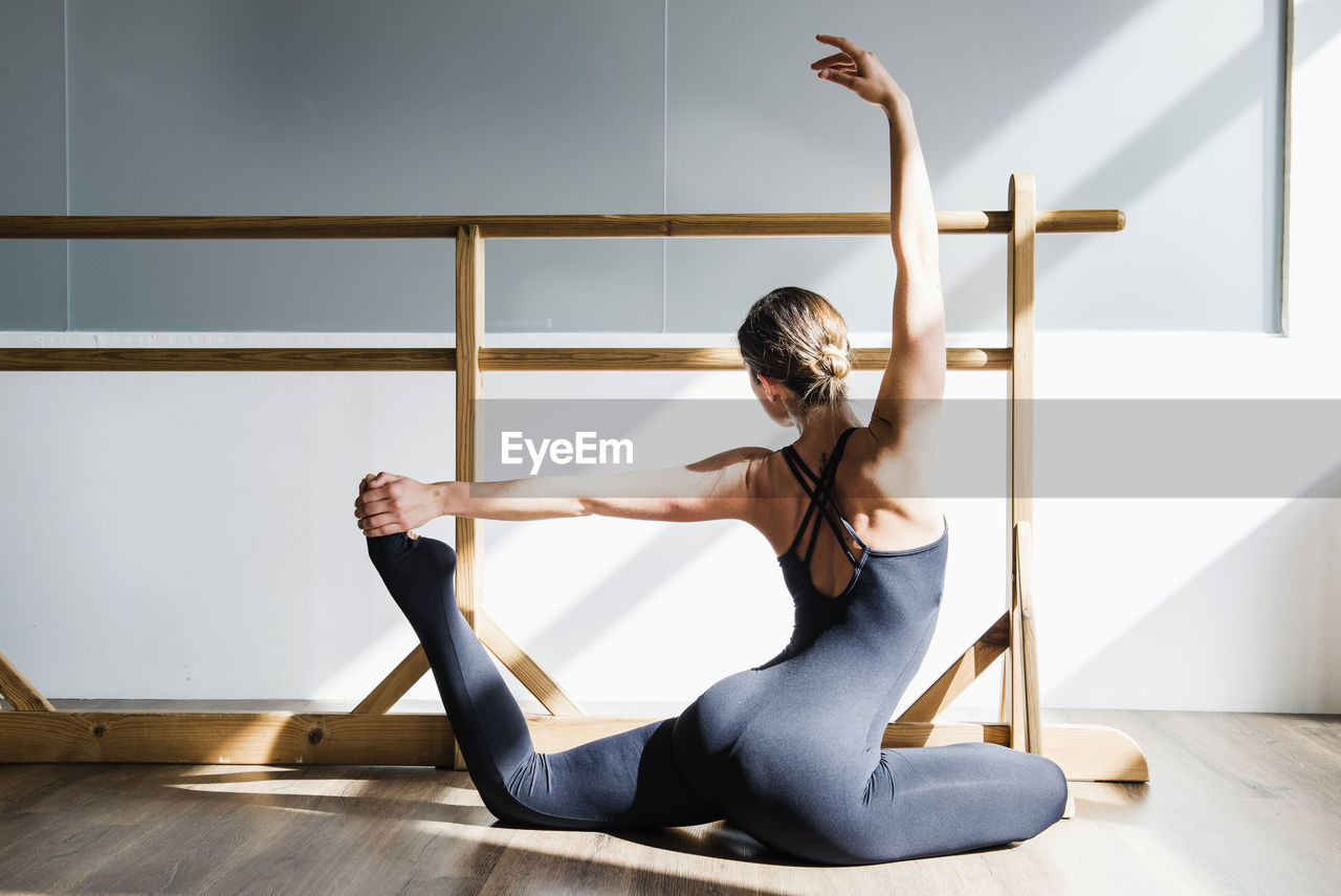 From behind view of anonymous young woman dancer doing a stretching routine on dance studio floor