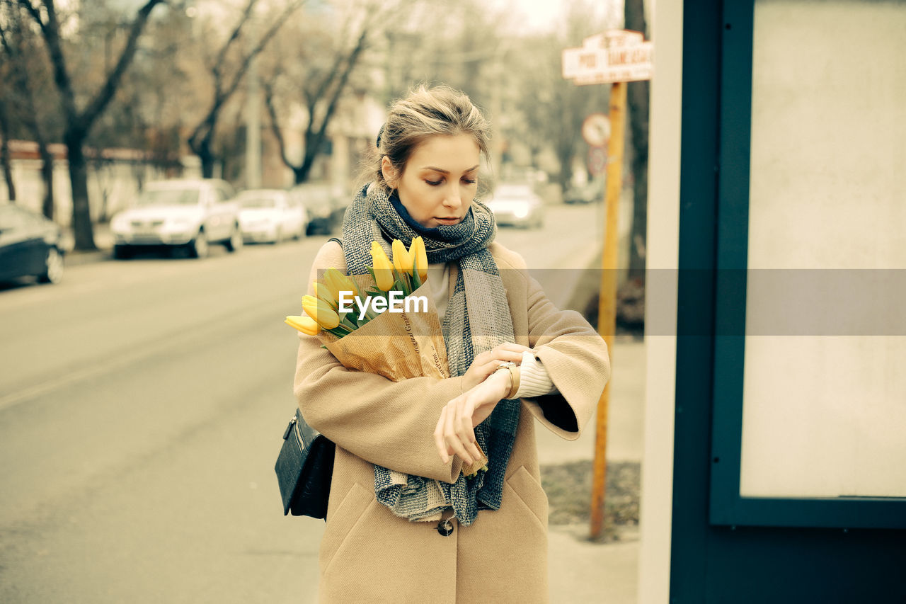 An attractive caucasian blonde woman  looking at her wristwatch while waiting for the bus.