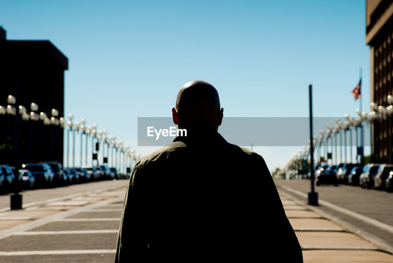 REAR VIEW OF MAN STANDING BY BRIDGE AGAINST SKY