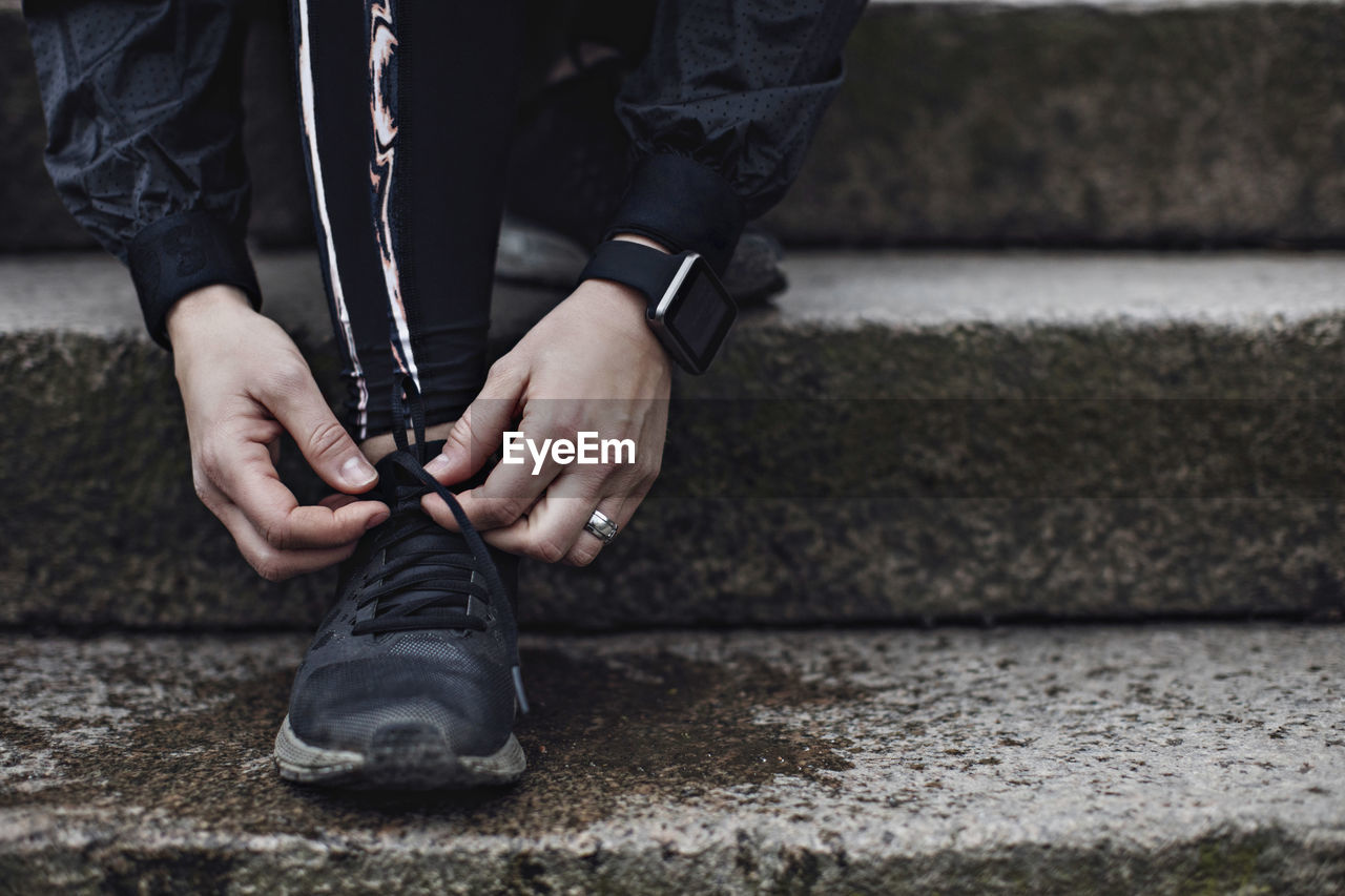 Low section of young woman tying shoelace on steps