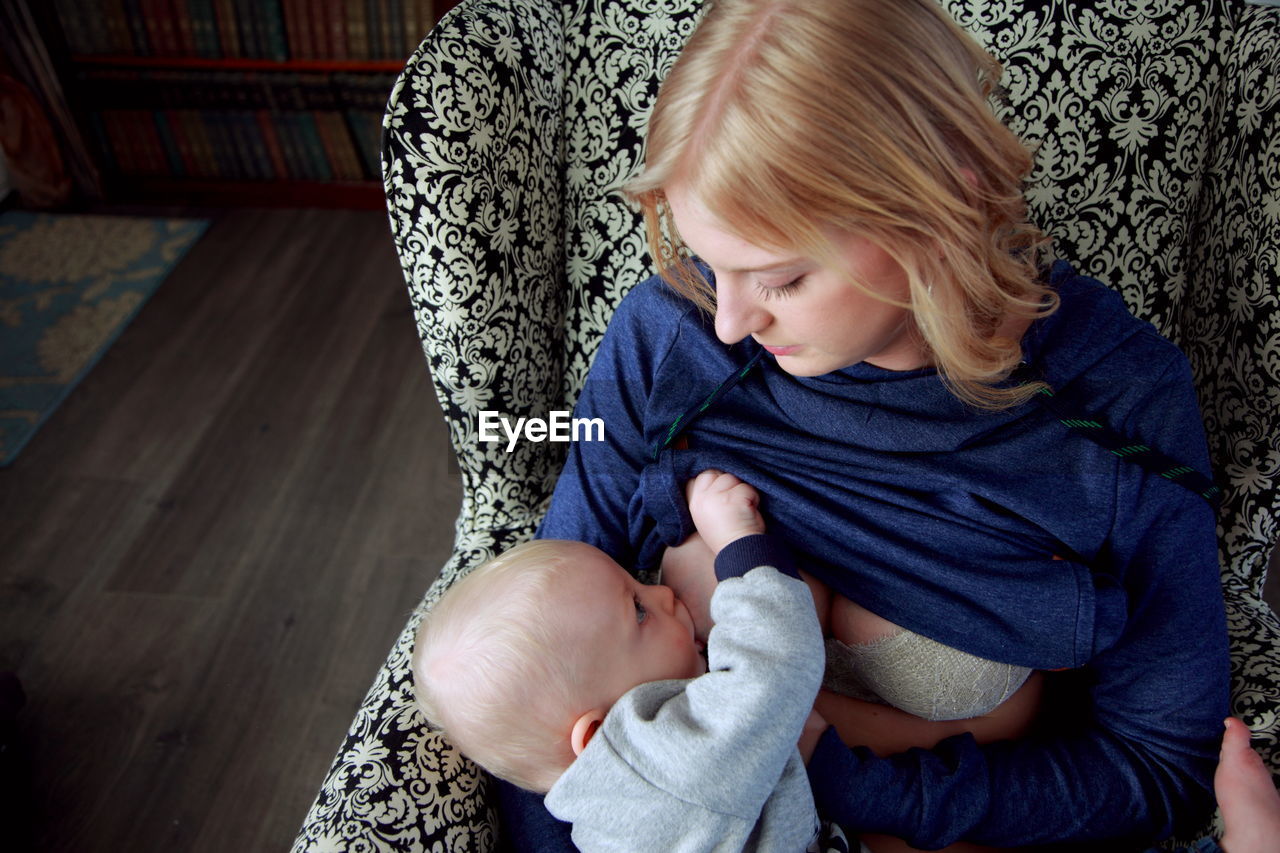 High angle view of mother breastfeeding son while sitting at home