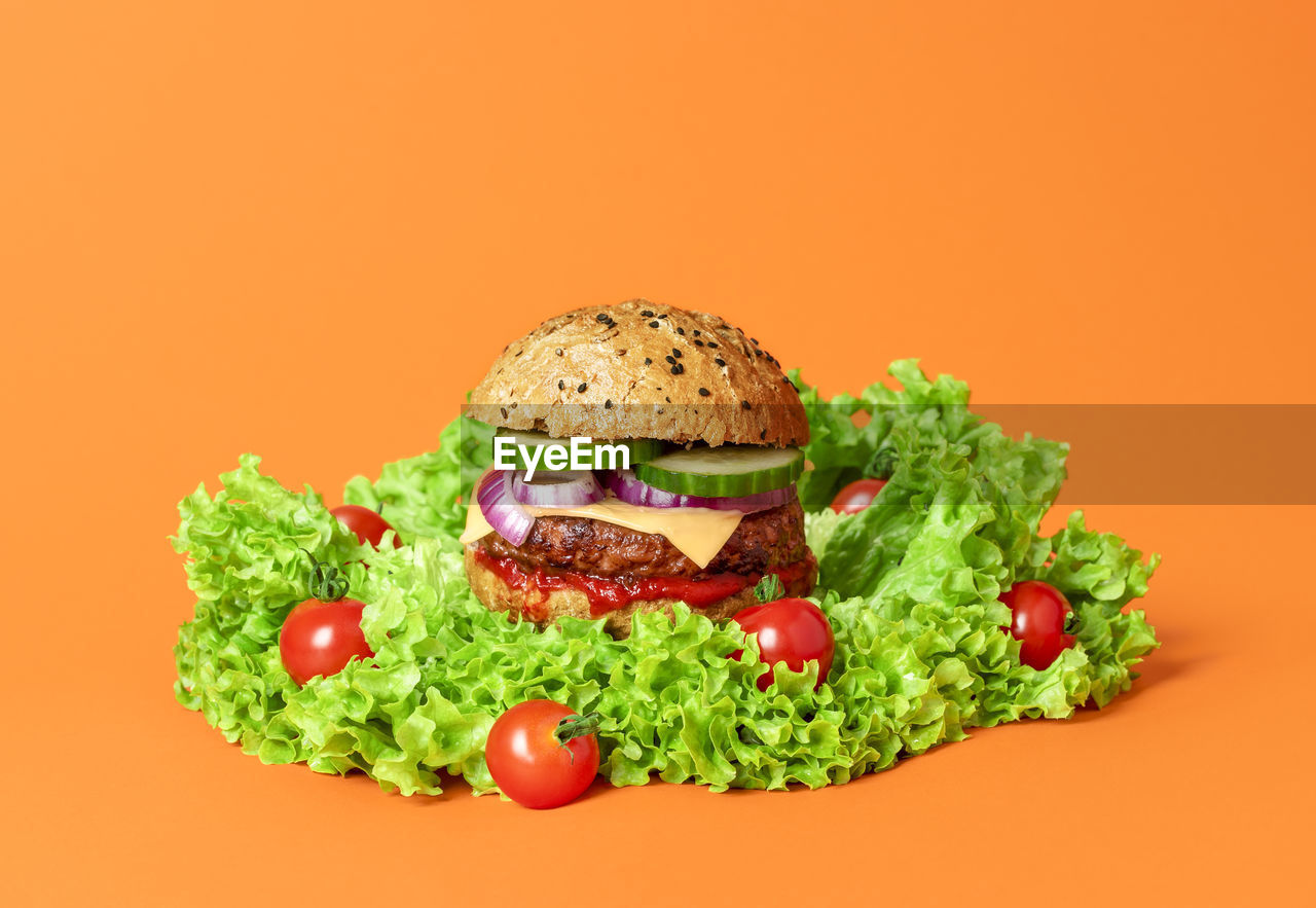 Vegan burger on green salad on orange background. cheeseburger with soya patty, cashew cheese