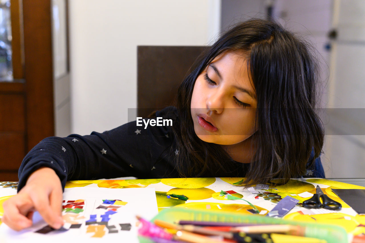 Little girl gluing colored papers for her homework