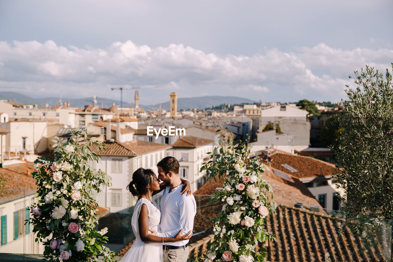 Newlywed couple embracing against cityscape