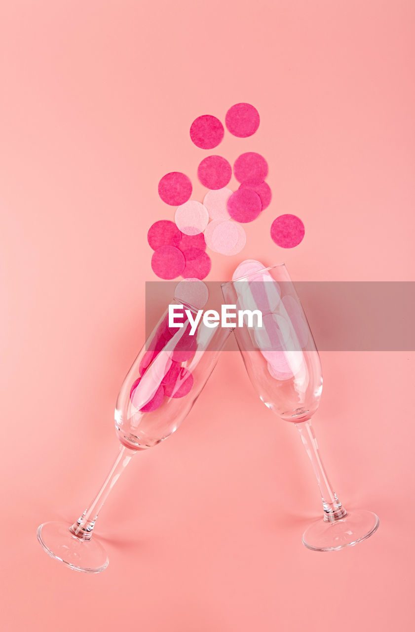 Holidays concept. pink confetti pouring out of the glass on pink background flat lay top view