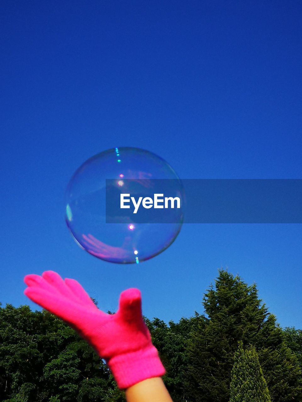 Cropped image of person reaching bubble against clear blue sky