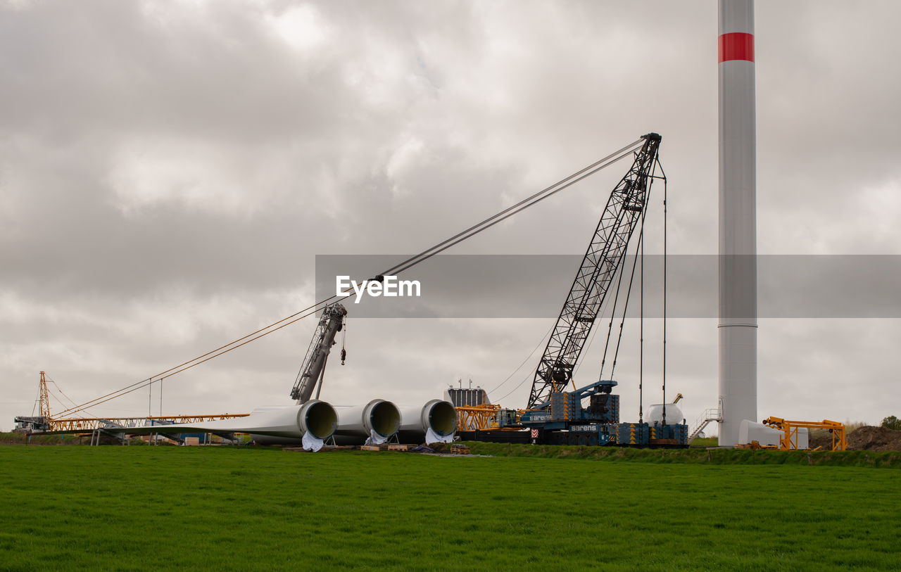 SCENIC VIEW OF FIELD BY CRANES AGAINST SKY