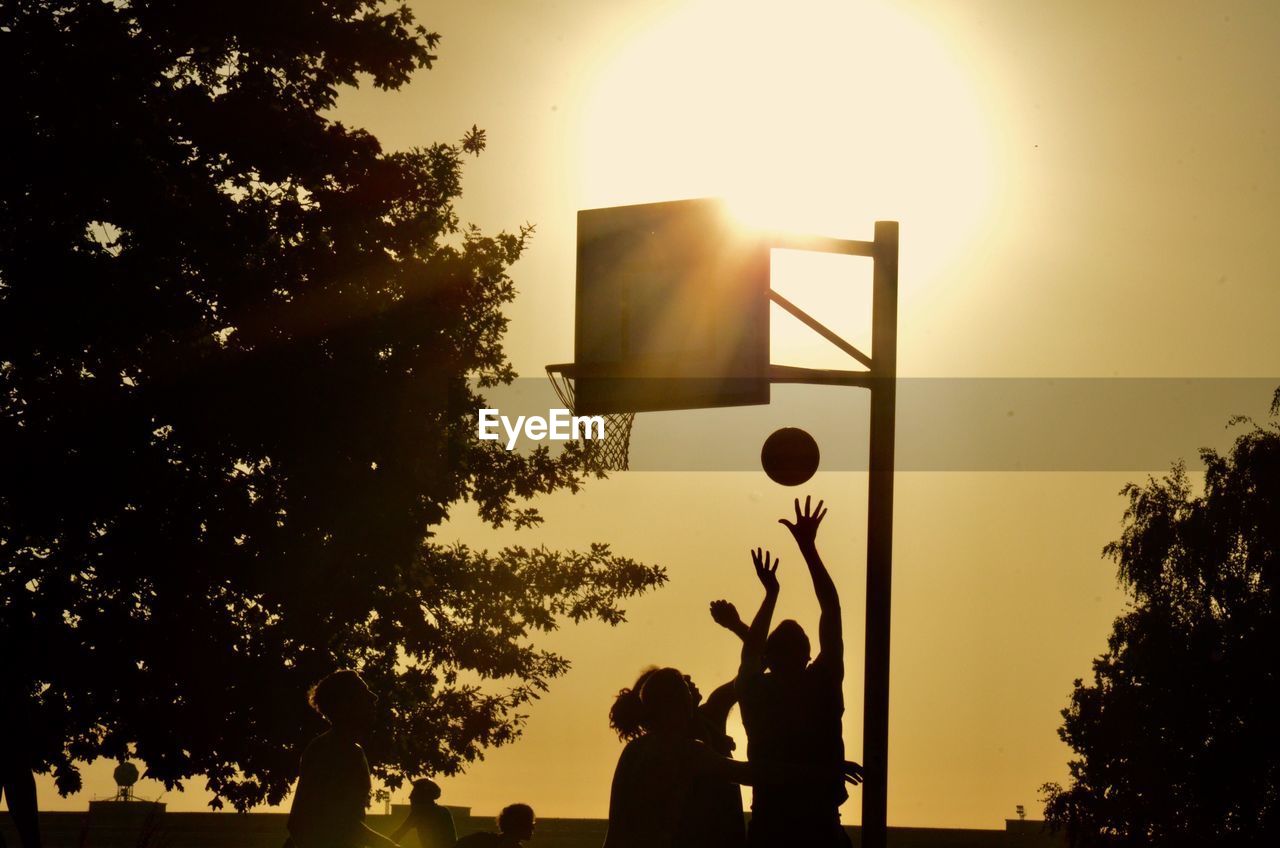 Silhouette people playing basketball against sky during sunset